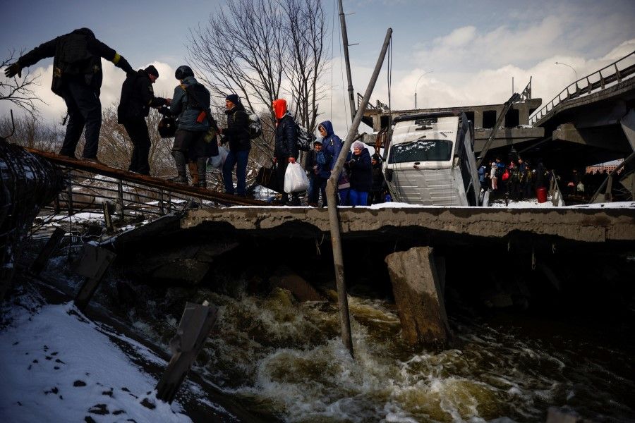 People file across a makeshift river crossing below a destroyed bridge as they flee from advancing Russian troops whose attack on Ukraine continues in the town of Irpin outside Kyiv, Ukraine, 8 March 2022. (Thomas Peter/Reuters)