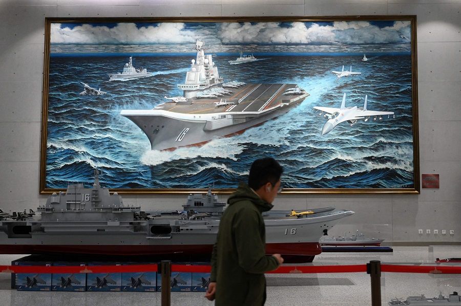 A man walks past a model and painting of China's Liaoning aircraft carrier at the Military Museum in Beijing, China, on 3 March 2024. (Greg Baker/AFP)