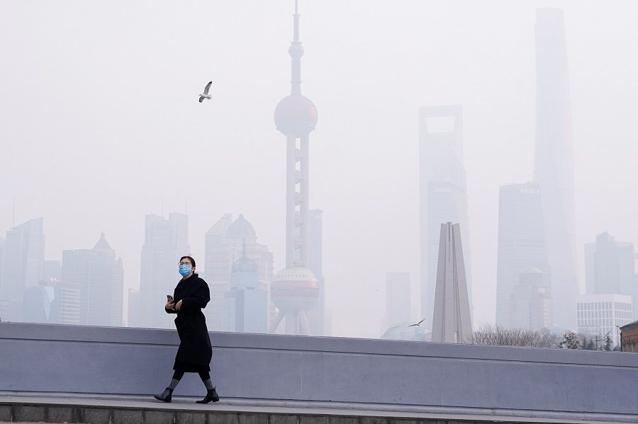 In this photo taken on 3 February 2020, a woman wearing a mask is seen on a bridge in front of the financial district of Pudong, Shanghai, China, as the country is hit by the Covid-19 pandemic. (Aly Song/Reuters)