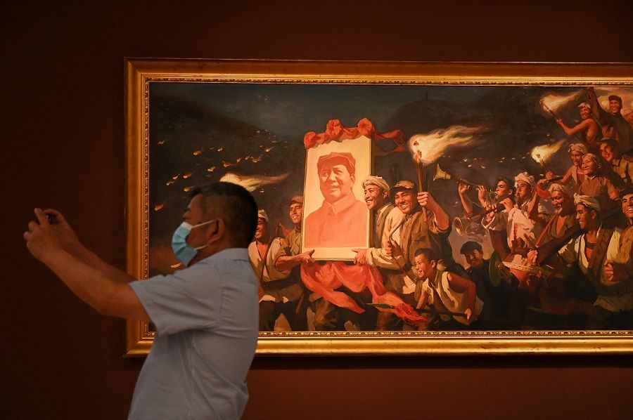 A man takes a photo in front of a painting of people carrying a poster of late communist leader Mao Zedong titled "Yan'an Torch", by artist Cai Liang, at an exhibition of art celebrating the 100th anniversary of the founding of the Communist Party in Beijing, China, on 24 June 2021. (Greg Baker/AFP)