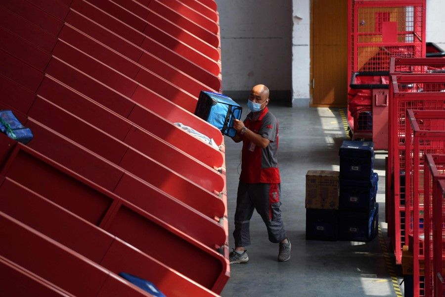A worker collects a package after it was delivered by an automated conveyer belt at a JD.com distribution center in Beijing on 16 July 2020. (Greg Baker/AFP)