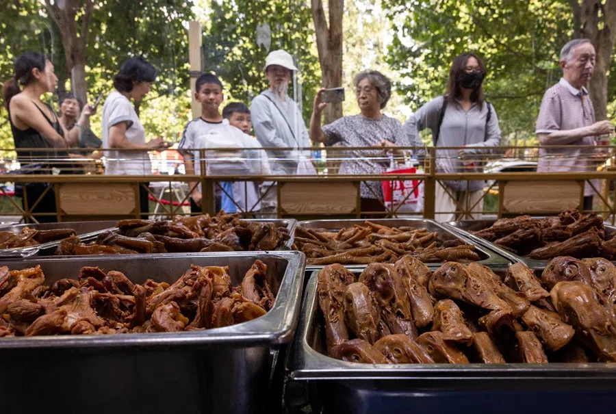 People queue next to metal trays filled with cooked poultry parts in Beijing, China on 11 August 2025. (Maxim Shemetov/Reuters)