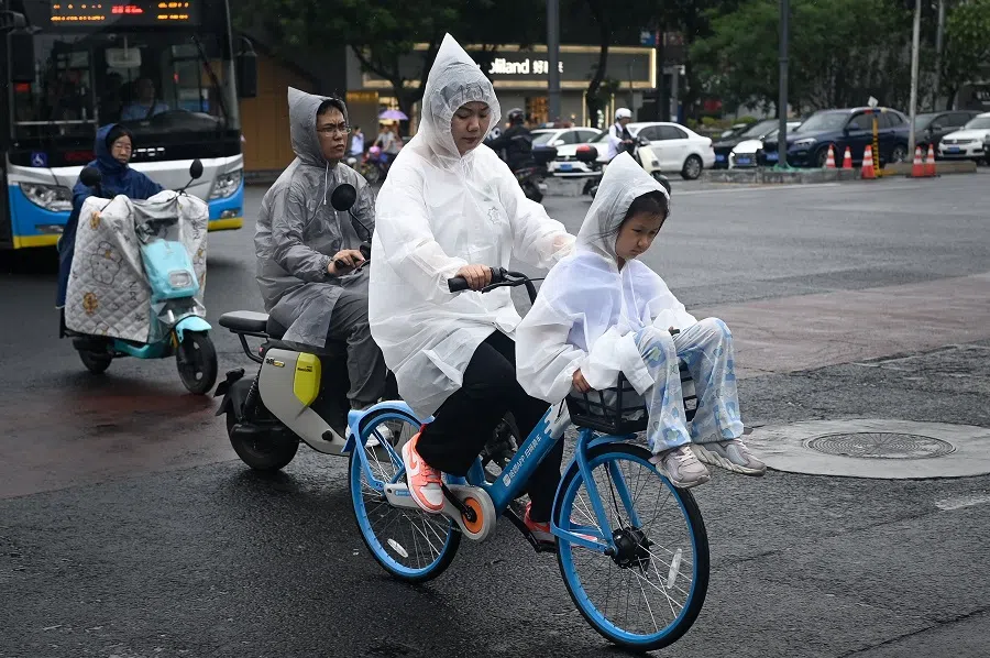 A raincoat-clad child rides in the front basket of a bicycle on a rainy day in Beijing on 2 July 2024.  (Wang Zhao/AFP)