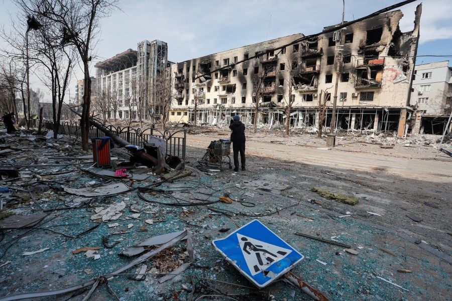 A resident stands with her belongings on a street near a building burnt in the course of the Ukraine-Russia conflict, in the southern port city of Mariupol, Ukraine, 10 April 2022. (Alexander Ermochenko/Reuters)