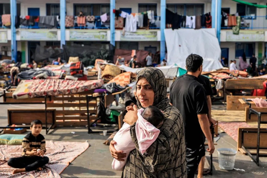 A woman walks carrying an infant in the playground of a school run by the United Nations Relief and Works Agency for Palestine Refugees agency that has been converted into a shelter for displaced Palestinians in Khan Yunis in the southern Gaza Strip on 25 October 2023, amid the ongoing battles between Israel and the Palestinian group Hamas. (Mahmud Hams/AFP)