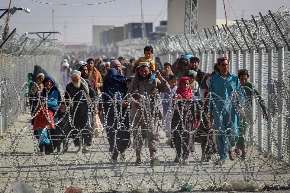 Afghans walk along fences as they arrive in Pakistan through the Pakistan-Afghanistan border crossing point in Chaman on 24 August 2021 following Taliban's military takeover of Afghanistan. (AFP)