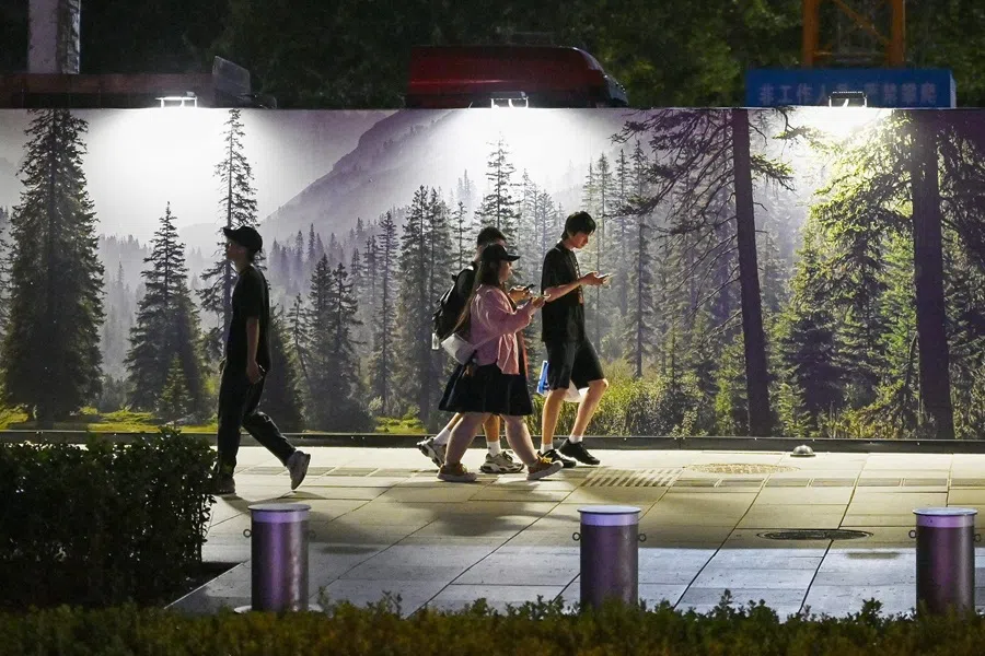 People walk past a construction site decorated with a forest scene in Beijing on 10 August 2025. (Greg Baker/AFP)