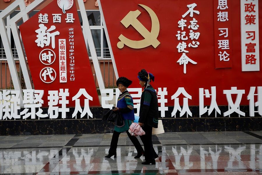 Ethnic Yi women walk past an installation featuring a logo of the Communist Party of China and numerous slogans at the Chengbei Gan'en Community, a residential complex built for a relocation programme as part of China's poverty alleviation effort, in Yuexi county, Liangshan Yi Autonomous Prefecture, Sichuan province, China, 11 September 2020. (Tingshu Wang/Reuters)