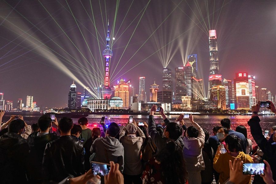 People wearing face masks on the Bund along the Huangpu River look at the light show seen in the Lujiazui financial district in Shanghai on 2 November 2020. (Hector Retamal/AFP)