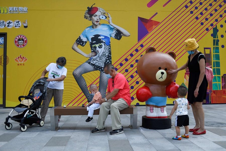 A group of people with young children relax along a pavement in Beijing on 23 July 2020. (Wang Zhao/AFP)