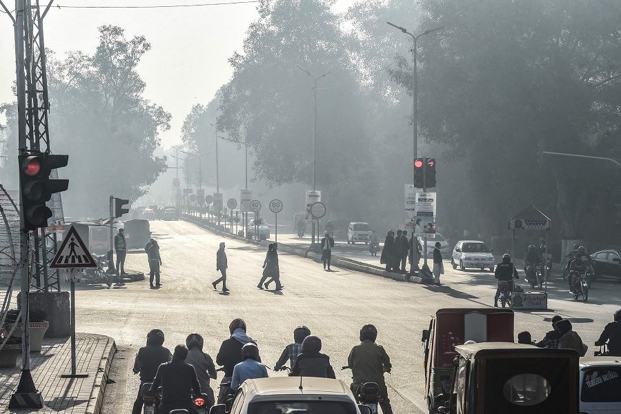 People cross a street in Lahore, Pakistan, on 23 November 2021. (Arif Ali/AFP)