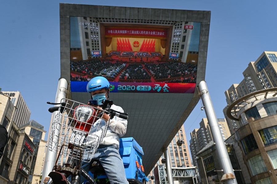 A food delivery man uses his mobile phone in front of a outdoor screen showing live coverage of the closing session of the National People's Congress (NPC) in Beijing, 28 May 2020. (Wang Zhao/AFP)