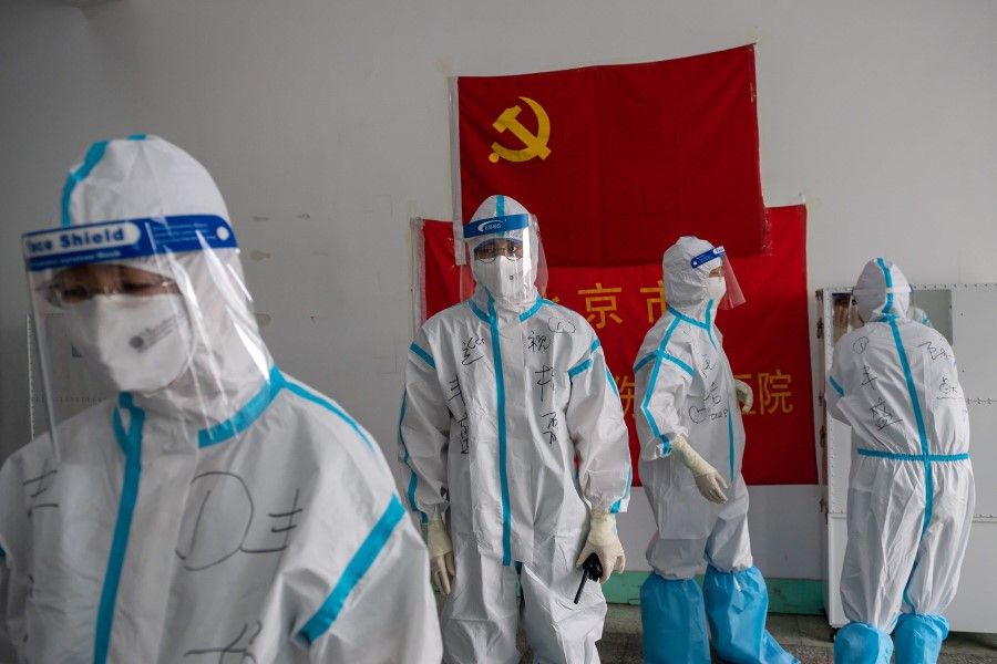 Medics from Beijing Fengsheng Special Hospital of Traditional Medical Traumatology and Orthopaedics prepare for their shift at the Jinrong Street testing site, inside a room where a Communist Party flag and a piece of red tissue with words that reads "Beijing Fengsheng Special Hospital of Traditional Medical Traumatology and Orthopaedics" (back on wall) in Beijing, 24 June 2020. (Nicolas Asfouri/AFP)