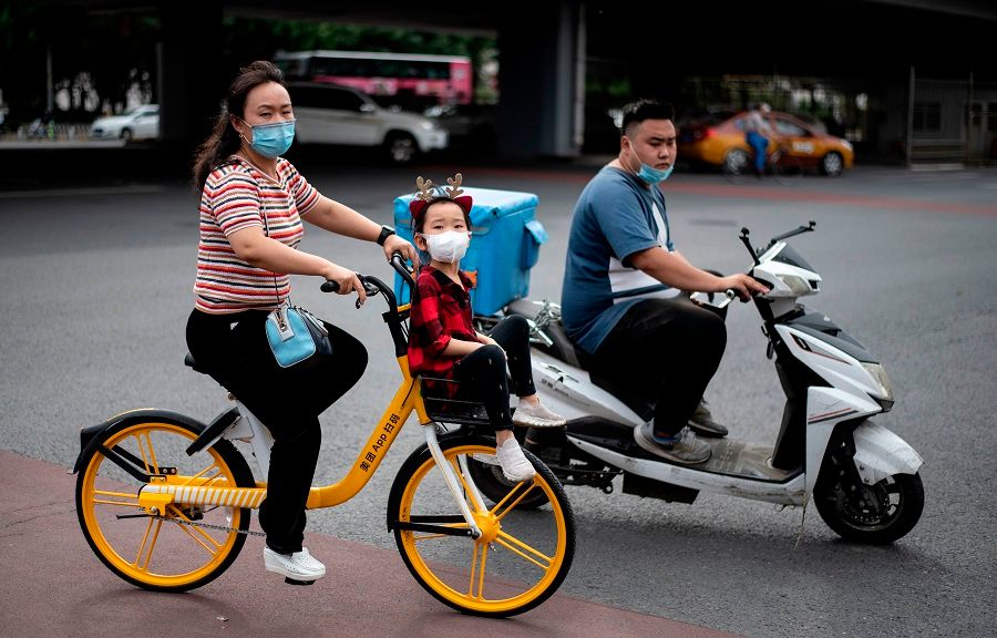 People wearing face masks cross a street on a bike in Beijing on 1 June 2020. (Noel Celis/AFP)