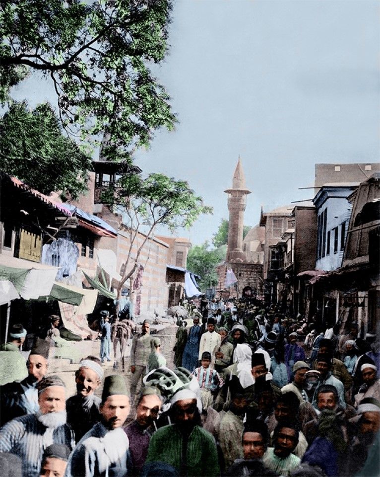 A crowded street in Damascus, 1880s. The men are wearing a cylindrical felt hat called a fez or tarboosh. In 1829, the Ottoman Empire began its reform and modernisation, and the fez took the place of traditional headcloths. On both sides of the street, vendors ply their wares. From ancient times, Damascus was a major transport channel, and a trading hub on the Silk Road.