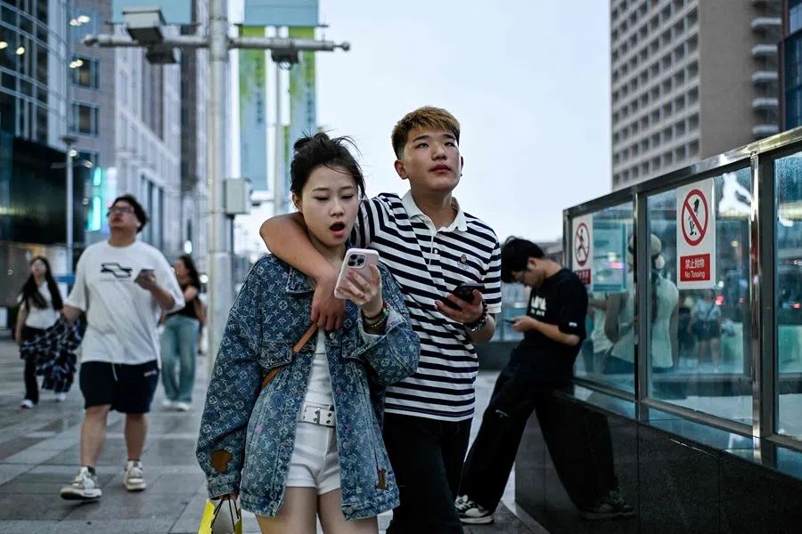 People stroll across a shopping street in Beijing on 19 August 2025. (Wang Zhao/AFP)