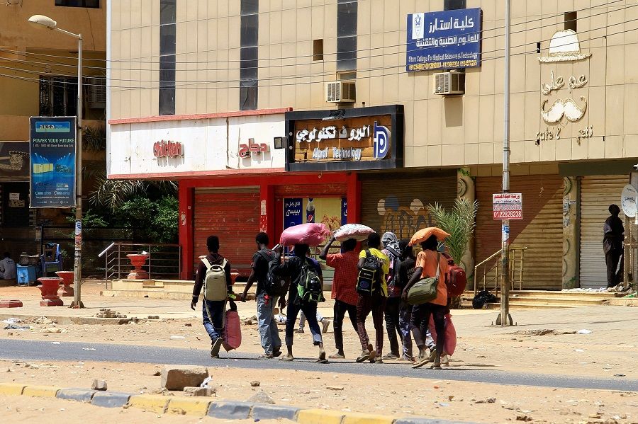 People carrying their belongings walk along a street in Khartoum, Sudan, on 16 April 2023, as fighting between the forces of two rival generals continues. (AFP)