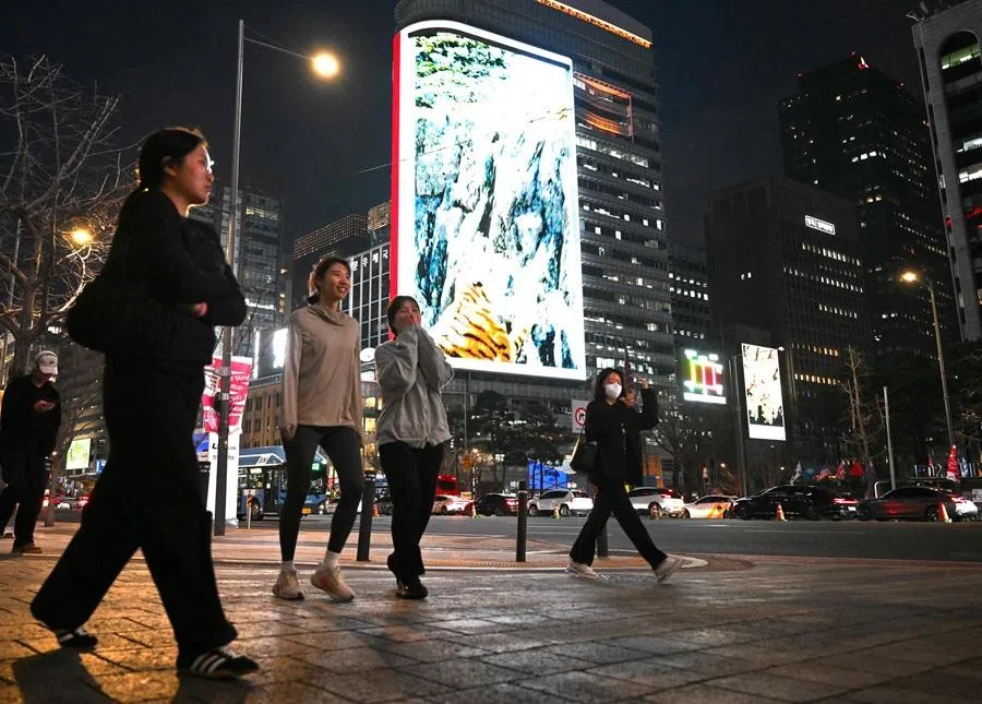 People walk in front of digital billboards near Gwanghwamun Square in Seoul on 1 April 2026.