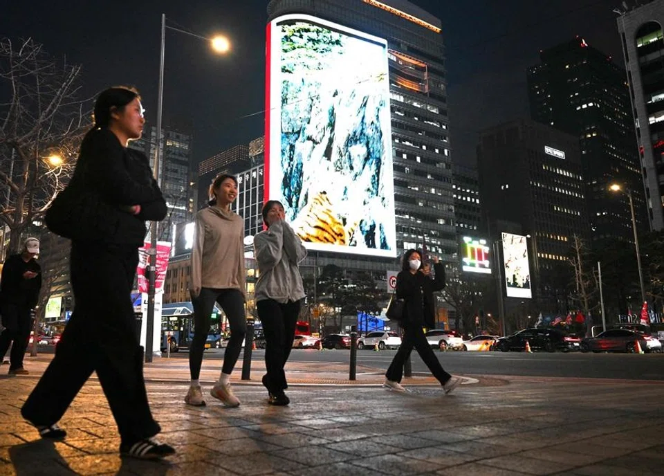People walk in front of digital billboards near Gwanghwamun Square in Seoul on 1 April 2026. (Jung Yeon-je/AFP)