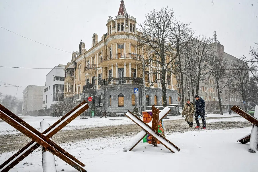 People walk along a snow covered street, past anti-tank hedgehogs in Kharkiv, Ukraine, on 18 February 2023, amid the Russian invasion of Ukraine. (Sergey Bobok/AFP)