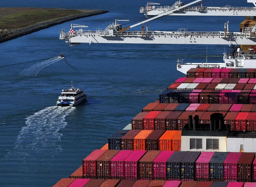 In an aerial view, a ferry boat passes a container ship docked at the Port of Oakland on 9 December 2024 in Oakland, California.  (Justin Sullivan/Getty Images via AFP)