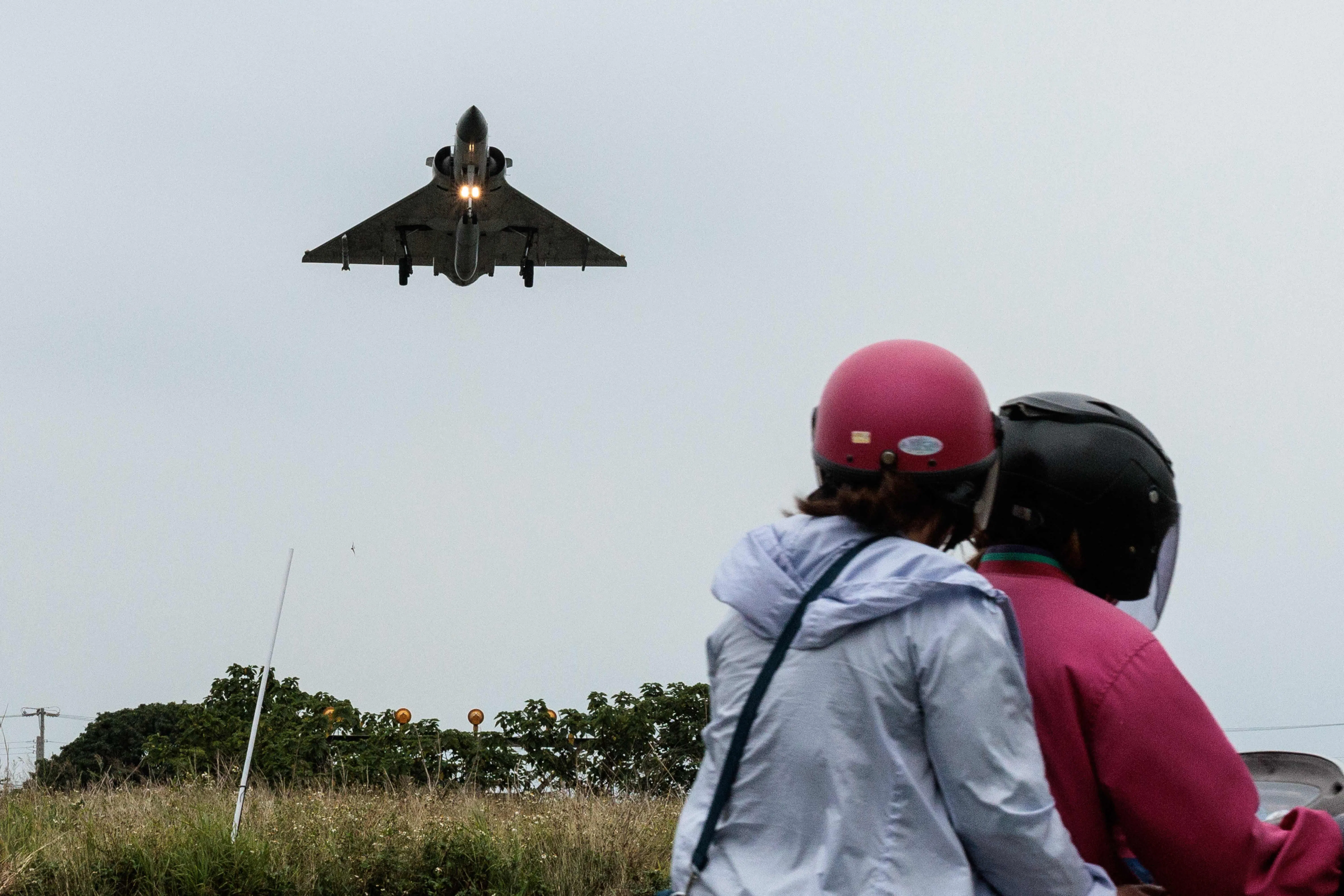 TOPSHOT - Two people ride a motorcycle as a Taiwanese Air Force Mirage 2000 fighter jet approaches for landing at an air force base in Hsinchu in northern Taiwan on 23 May 2024. (Yasuyoshi Chiba/AFP)