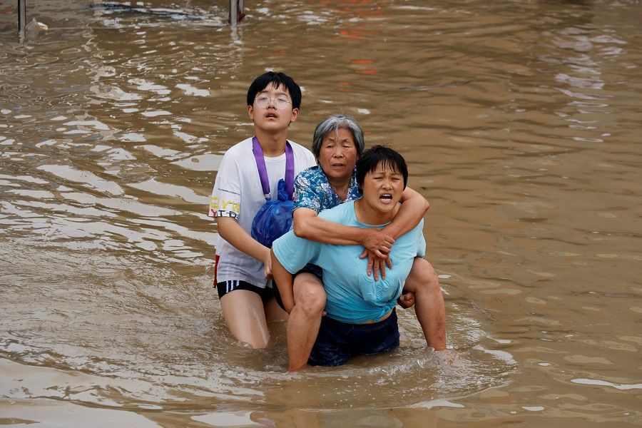 A woman carries an elderly woman as they make their way through floodwaters following heavy rainfall in Zhengzhou, Henan province, China, 23 July 2021. (Aly Song/Reuters)