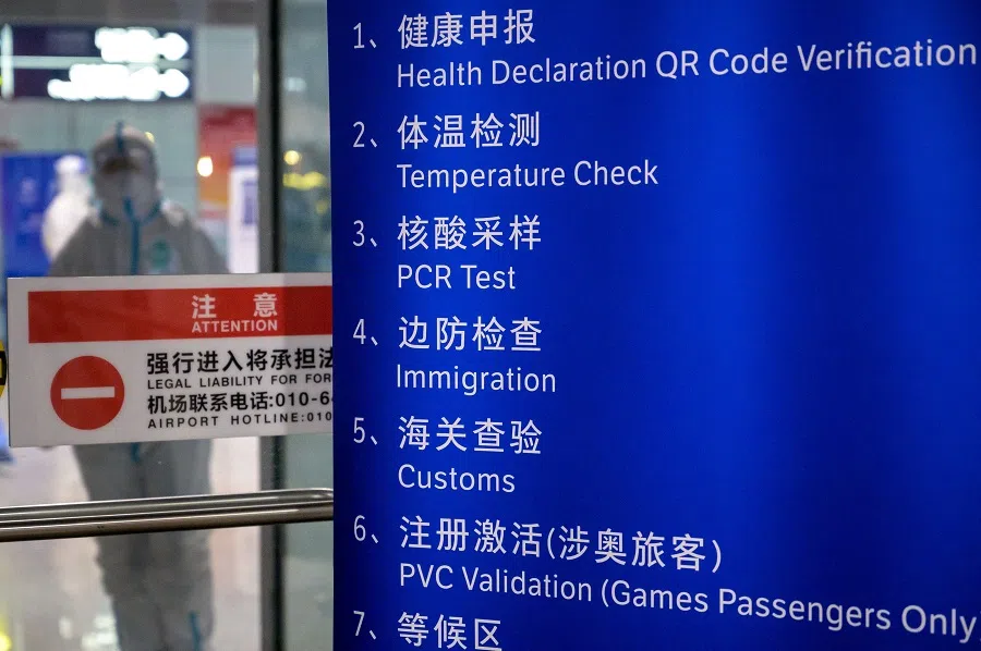A worker in a hazmat suit stands behind a board at a disembarkment door at the Beijing Capital International Airport ahead of the 2022 Winter Olympics in Beijing, China, on 27 January 2022. (Fabrice Coffrini/AFP)