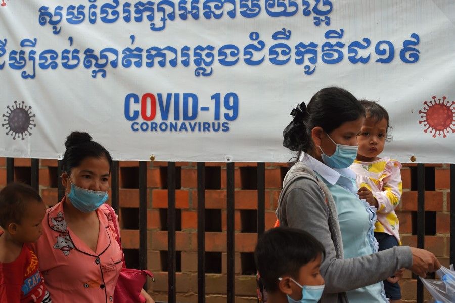 Women wearing face masks amid concerns over the spread of the Covid-19 coronavirus, carry their child outside a hospital with a banner warning about the virus in Phnom Penh on 29 September 2020. (Tang Chhin Sothy/AFP)
