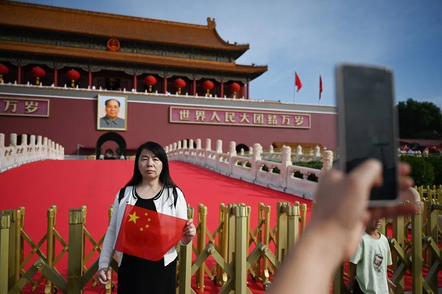 A woman poses for photos with the national flag in Tiananmen Square in Beijing on 1 October 2025. (Greg Baker/AFP)