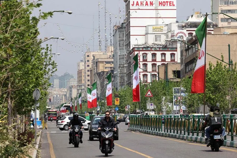 Vehicles and motorbikes drive along a street adorned with the Iranian flag, in Tehran on 21 April 2026, amid a ceasefire in the region. (Atta Kenare/AFP)