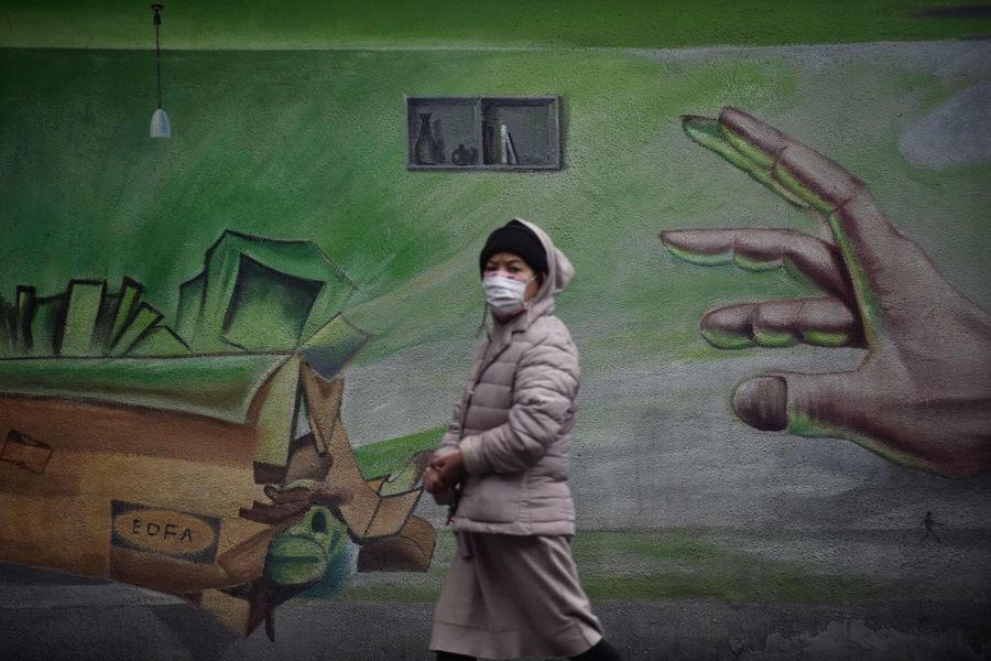 This photo taken on 28 February 2020 shows a resident walking past a mural in Wuhan. (STR/AFP)