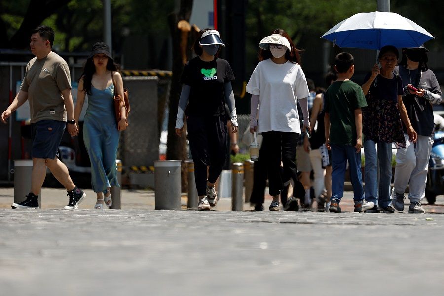 People wearing sun-protective clothing cross a road amid a yellow alert for heatwave in Beijing, China, 5 June 2023. (Florence Lo/Reuters)