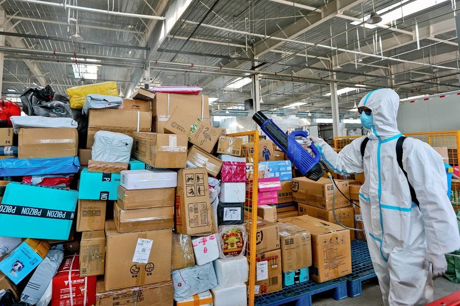This photo taken on 16 November 2021 shows a staff member spraying disinfectant on packages to be delivered as a preventive measure against the Covid-19 coronavirus, at a logistics company in Zhangye, Gansu province, China. (AFP)