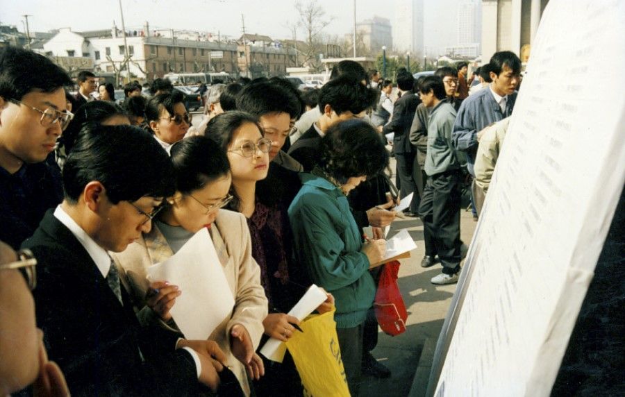 Young people in Shanghai look at job recruitment advertisements, 1997. China underwent reforms and no longer assigned jobs to university graduates; they had to find jobs on their own.