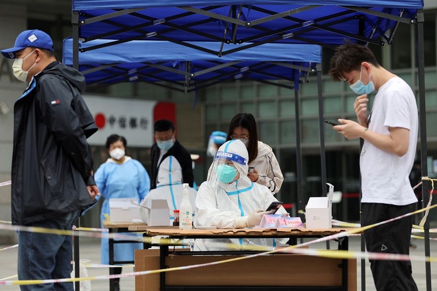 A worker in a protective suit registers information for people lining up at a makeshift nucleic acid testing site during a mass testing for Covid-19 in Chaoyang district of Beijing, China, 10 May 2022. (Tingshu Wang/Reuters)