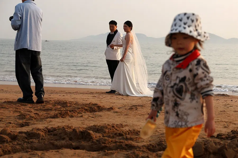 A child plays with sand near a couple taking part in a pre-wedding photoshoot on a beach in Qingdao, Shandong province, China, on 21 April 2024.