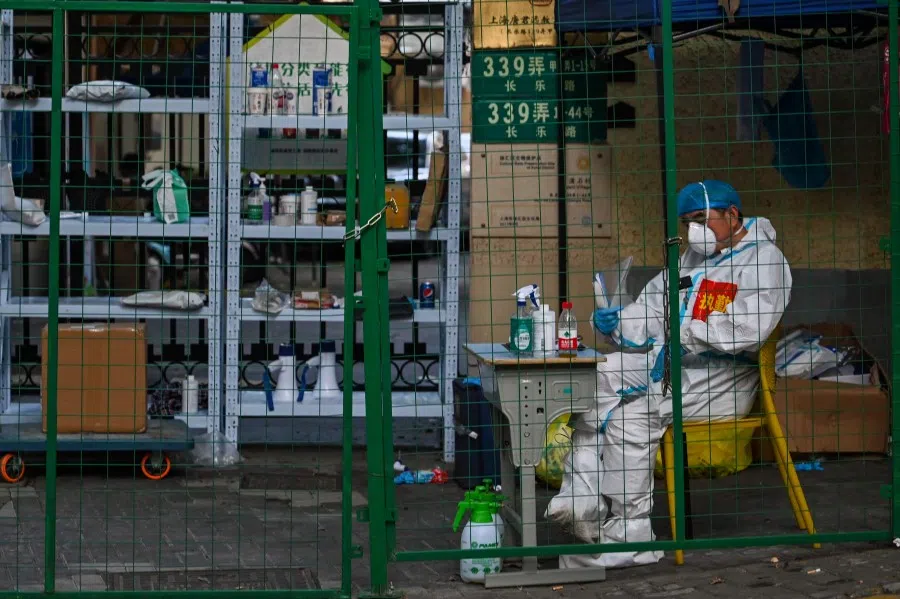 A worker wearing personal protective equipment (PPE) sits behind a fence in a residential area under a Covid-19 lockdown in the Xuhui district of Shanghai on 16 June 2022. (Hector Retamal/AFP)