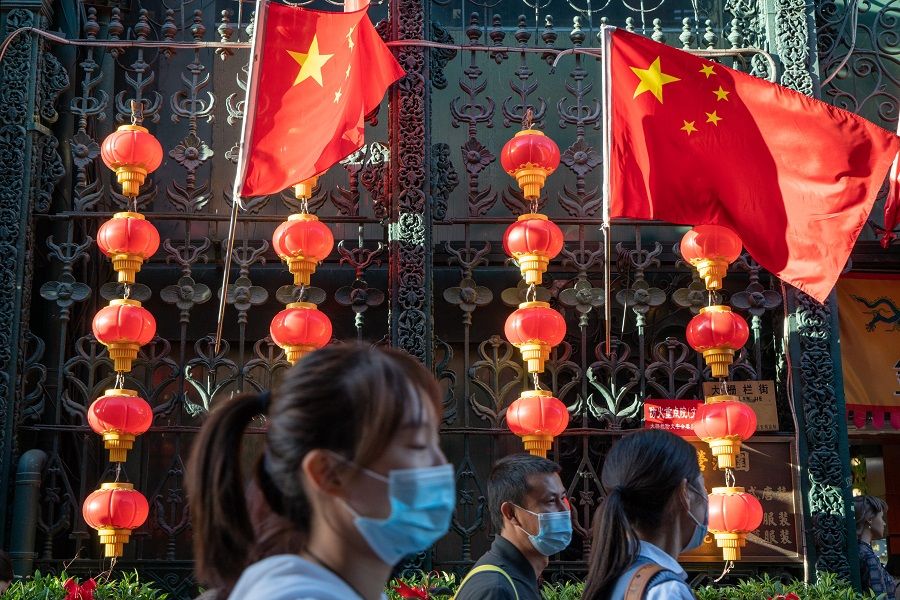 Visitors wearing protective masks walk by Chinese national flags and red lanterns decorated to celebrate the National Day in Beijing, China, 4 October 2020. (Yan Cong/Bloomberg)