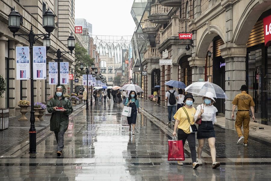 Pedestrians wearing protective masks walk with umbrellas past stores in Wuhan, China, on 30 April 2020. (Qilai Shen/Bloomberg)