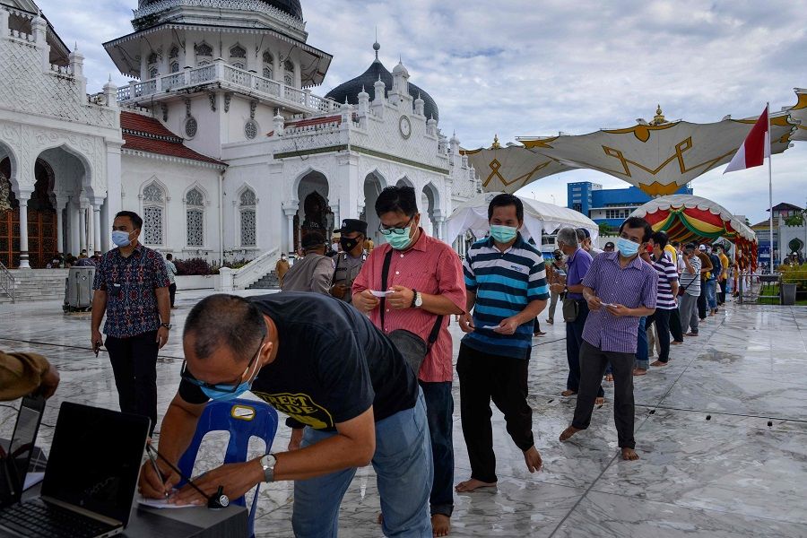 People wait in a queue before receiving the Sinovac Covid-19 vaccine in front of the Baiturrahman Grand Mosque in Banda Aceh, Indonesia, on 30 March 2021. (Chaideer Mahyuddin/AFP)