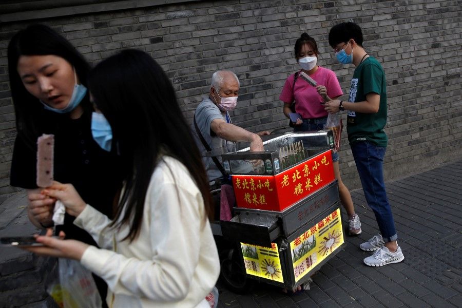 An elderly man attends to customers at his street stall selling traditional snacks in Beijing, 5 June 2020. (Tingshu Wang/REUTERS)