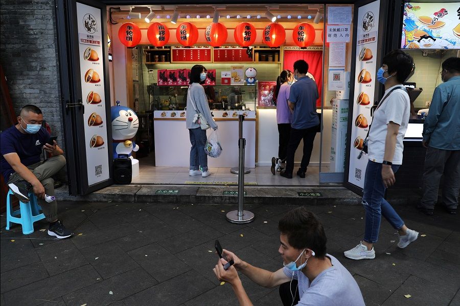 People look at their smartphones as others walk past the Nanluoguxiang alley in Beijing, China, 20 August 2021. (Tingshu Wang/Reuters)