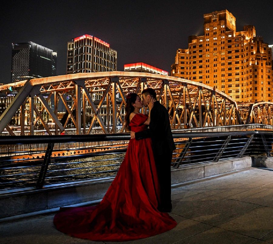 A couple posing for pictures next to the Garden Bridge of Shanghai, in the Huangpu district in Shanghai on 6 December 2023. (Hector Retamal/AFP)