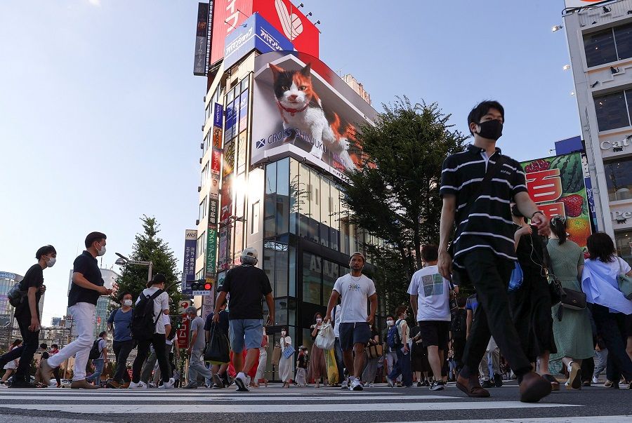 Passersby wearing protective face masks walks on the street at Shinjuku district in Tokyo, Japan, 1 August 2021. (Issei Kato/Reuters)