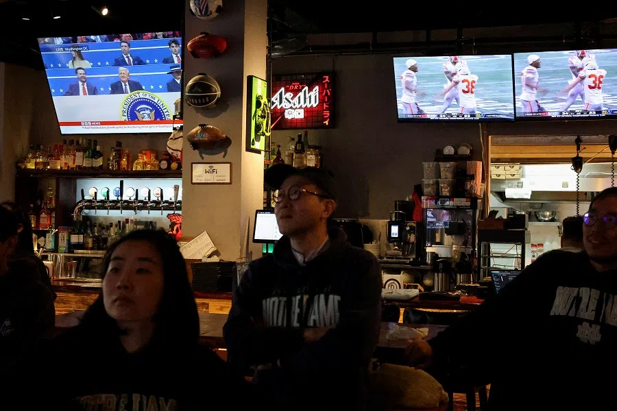 News about US President Donald Trump is shown on a TV screen as people watch American College Football, at a sports bar in Shanghai, China, on 21 January 2025. (Go Nakamura/Reuters)