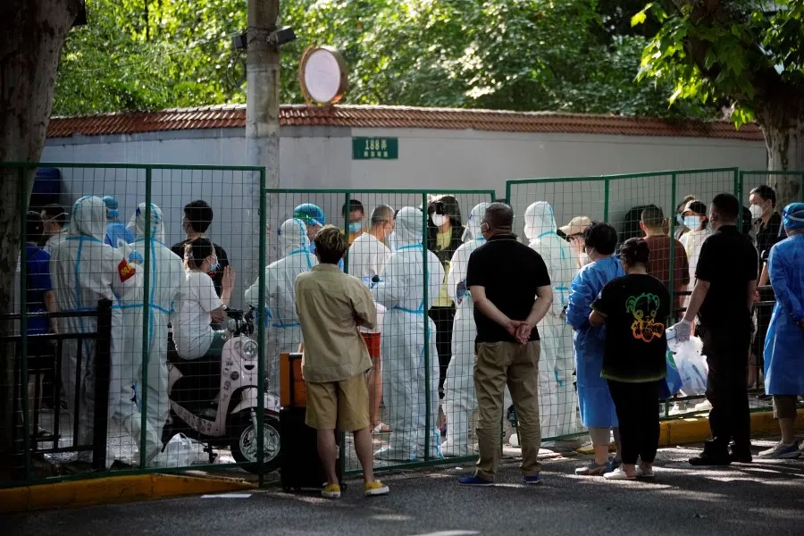 Residents wearing protective masks talk to security personnel and workers in protective suits in a fenced up area where restrictions to curb Covid-19 are in place, in Shanghai, China, 6 June 2022. (Aly Song/Reuters)