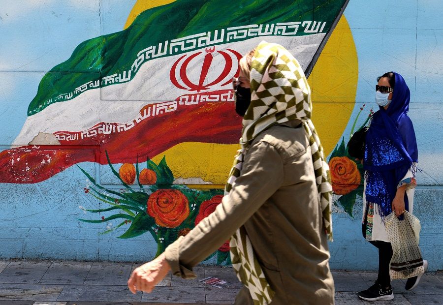 People wearing face masks walk past a mural displaying Iran's national flag in Tehran, Iran on 17 June 2021. (Atta Kenare/AFP)