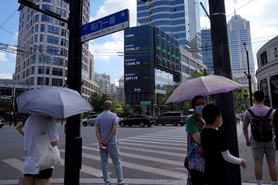 Pedestrians wait to cross a road at a junction near a giant display of stock indexes in Shanghai, China, 3 August 2022. (Aly Song/Reuters)