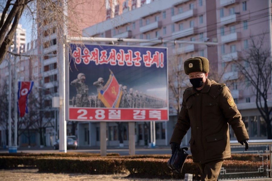 In a photo taken on 8 February 2021, a Korean People's Army (KPA) soldier walks past a poster displayed on a street in Pyongyang marking the 73rd anniversary of the foundation of the Korean People's Army. (Kim Won Jin/AFP)